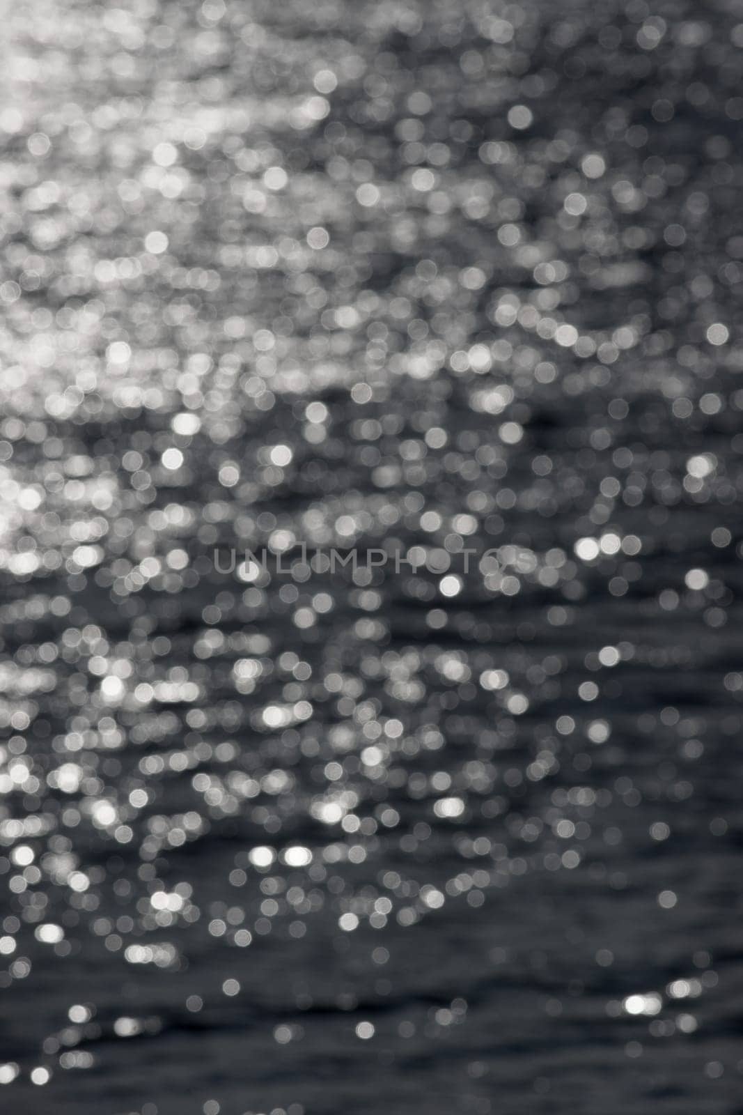 5 - Defocused vertical image of sunny water ripples, forming an abstract textured plain background of random white bokeh circles. Water theme.
