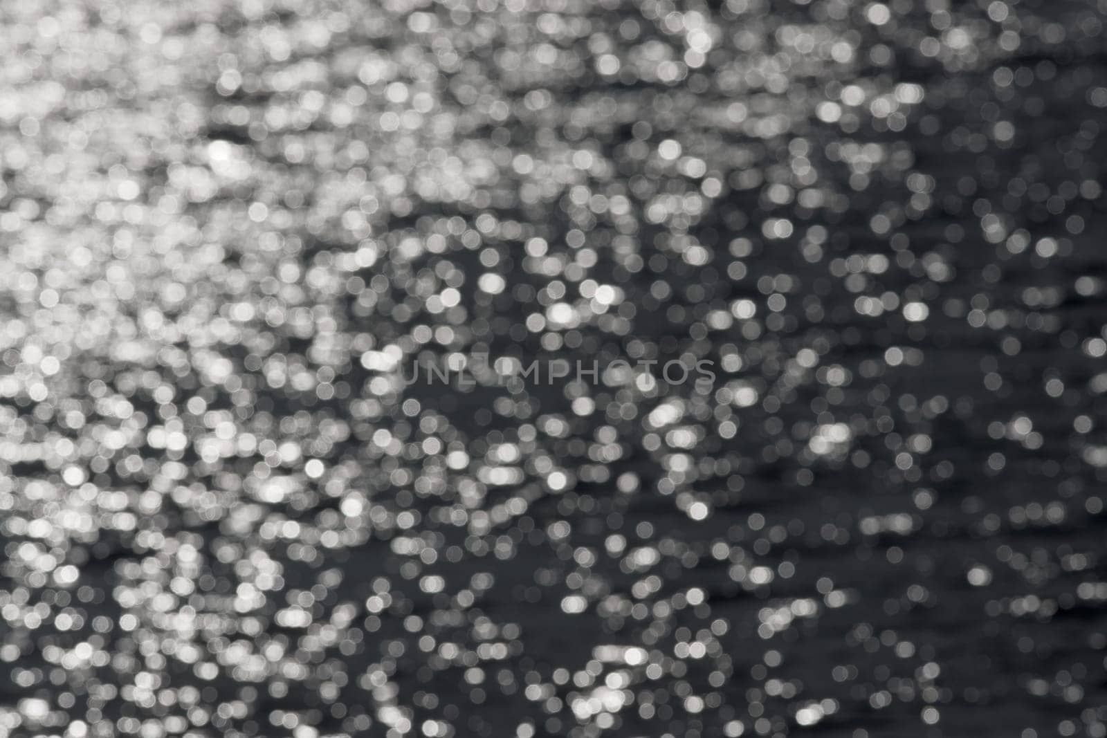 1 - Full frame sparkling out of focus spikes of light, formed from sunlight hitting ripples on a reservoir. monochrome dark grey against white.