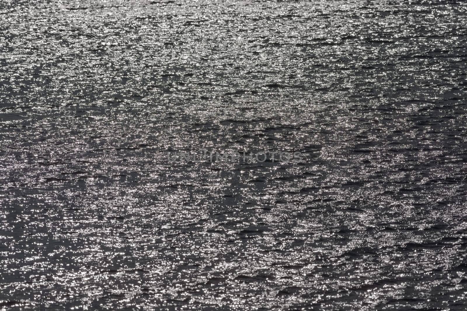 1 - Full frame sunlight shining off surface ripples of large reservoir lake. Glittery shimmer effect. monochrome grey with bright sun flare spots.