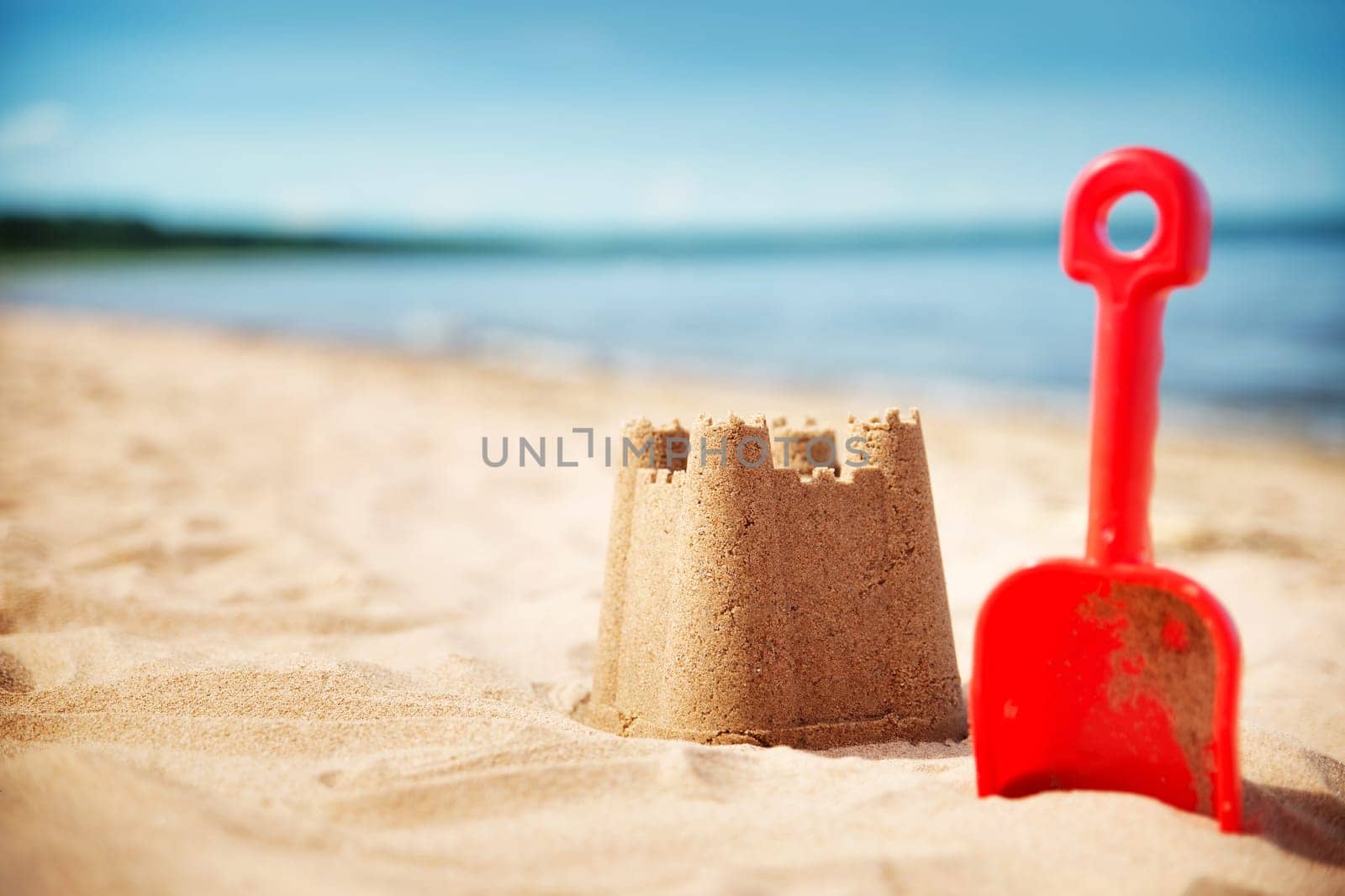 Sandcastle with a shovel on the sea in summertime. Seashore on beautiful day. Sand on the beach and blue water