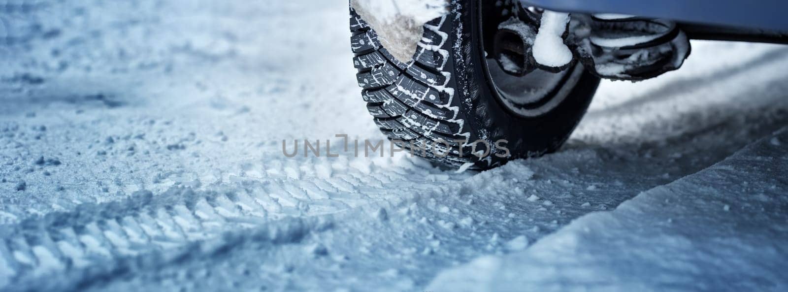 Car tires on winter road covered with snow. Panoramic view to vehicle on snowy way after snowfall