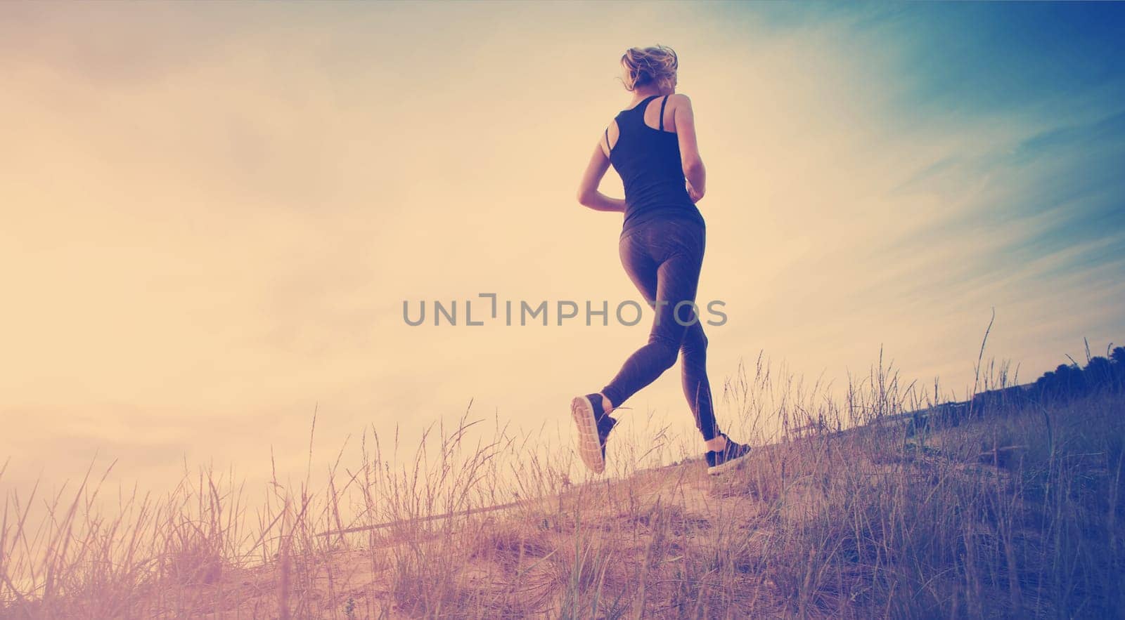 Young woman running on the field near seaside at sunset. Active person outdoors at the dusk in summer