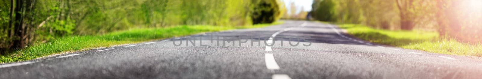 asphalt road panorama in countryside on sunny spring day.. Route in beautiful nature landscape with sun and green grass