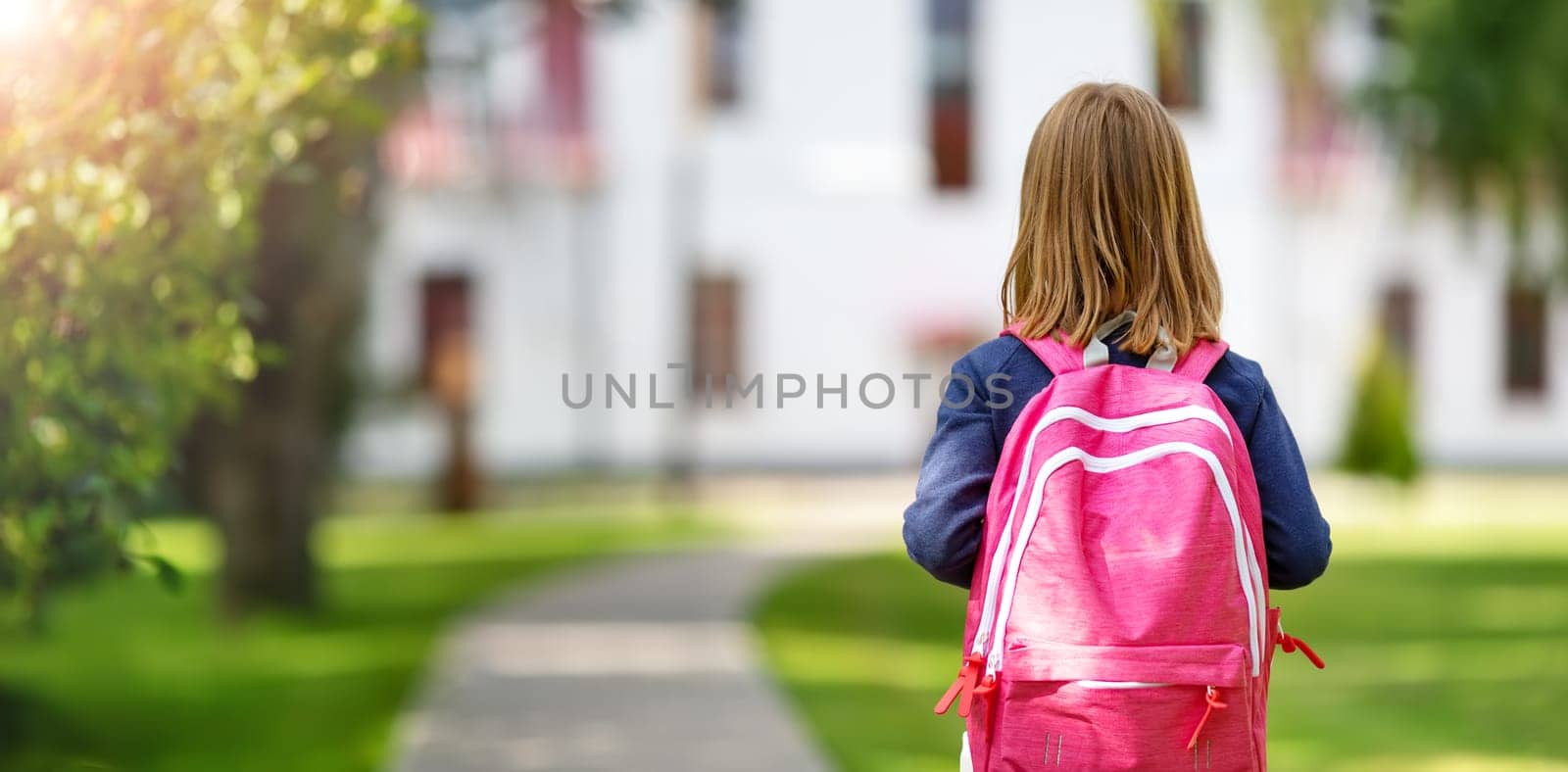 Girl with rucksack infront of a school building. Child with a backpack