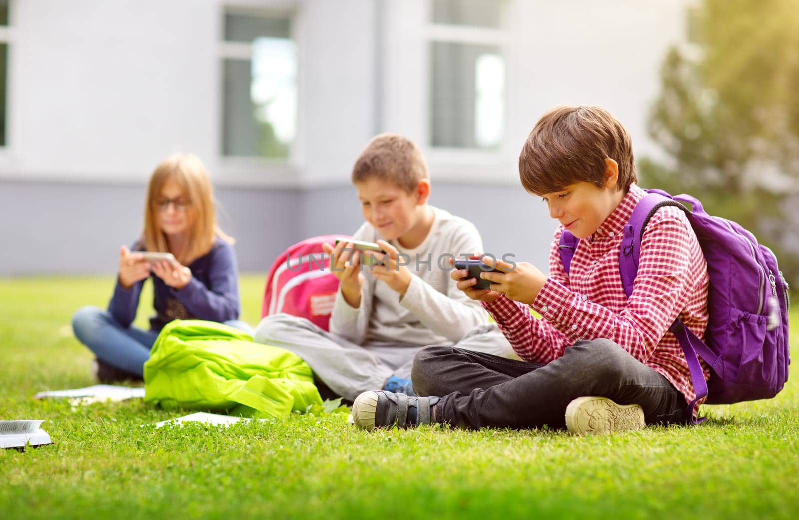 Children with rucksacks sitting in the park near school. Pupils with books and backpacks outdoors