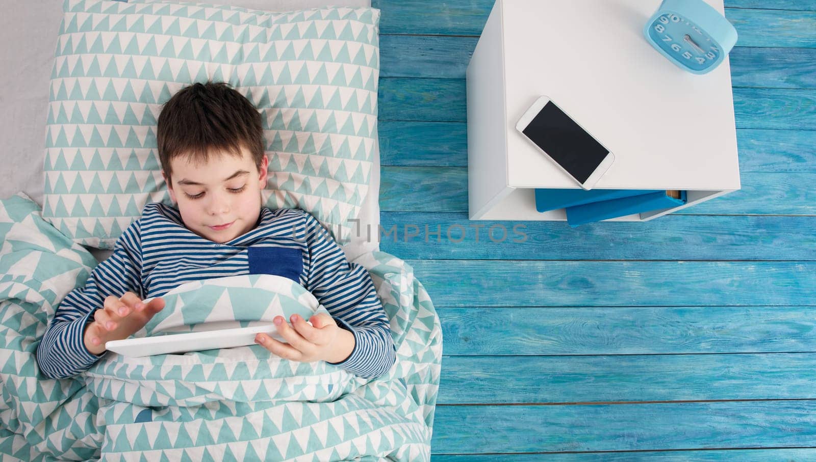 eight years old child sleeping in bed on pillow. Boy lying blue wooden background with smartphone and tablet