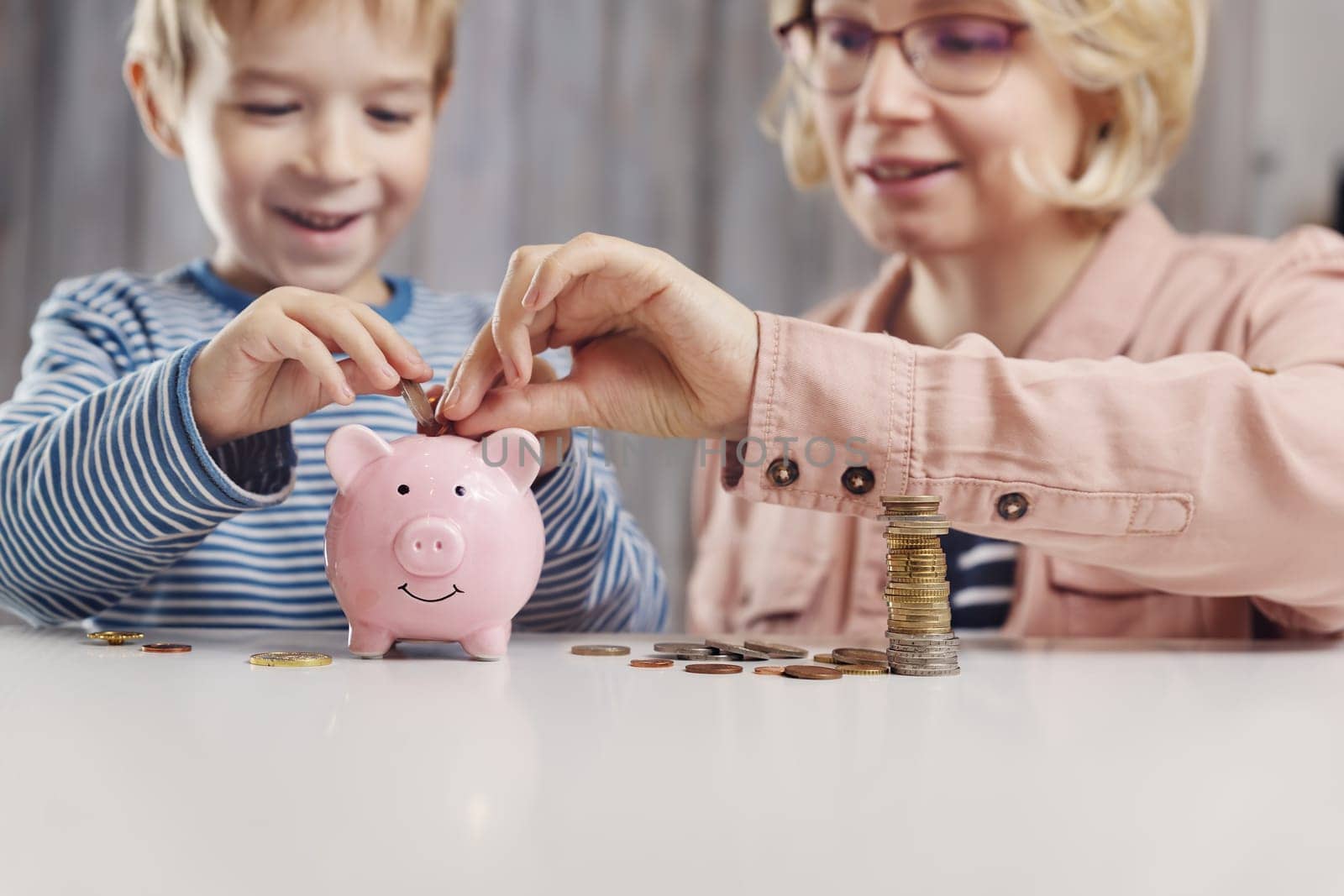 three years old child and young woman sitting at the table with money and piggybank. Happy boy with euro coins. Future childhood and education investment. Finance and savings concept. Son playing with mother