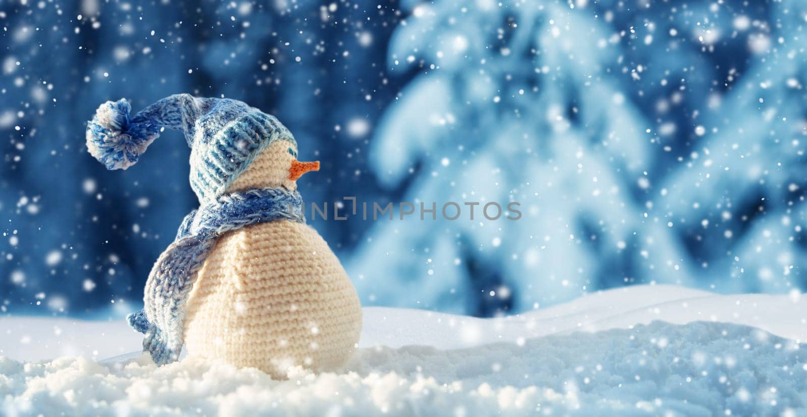little knitted snowman on soft snow on blue background