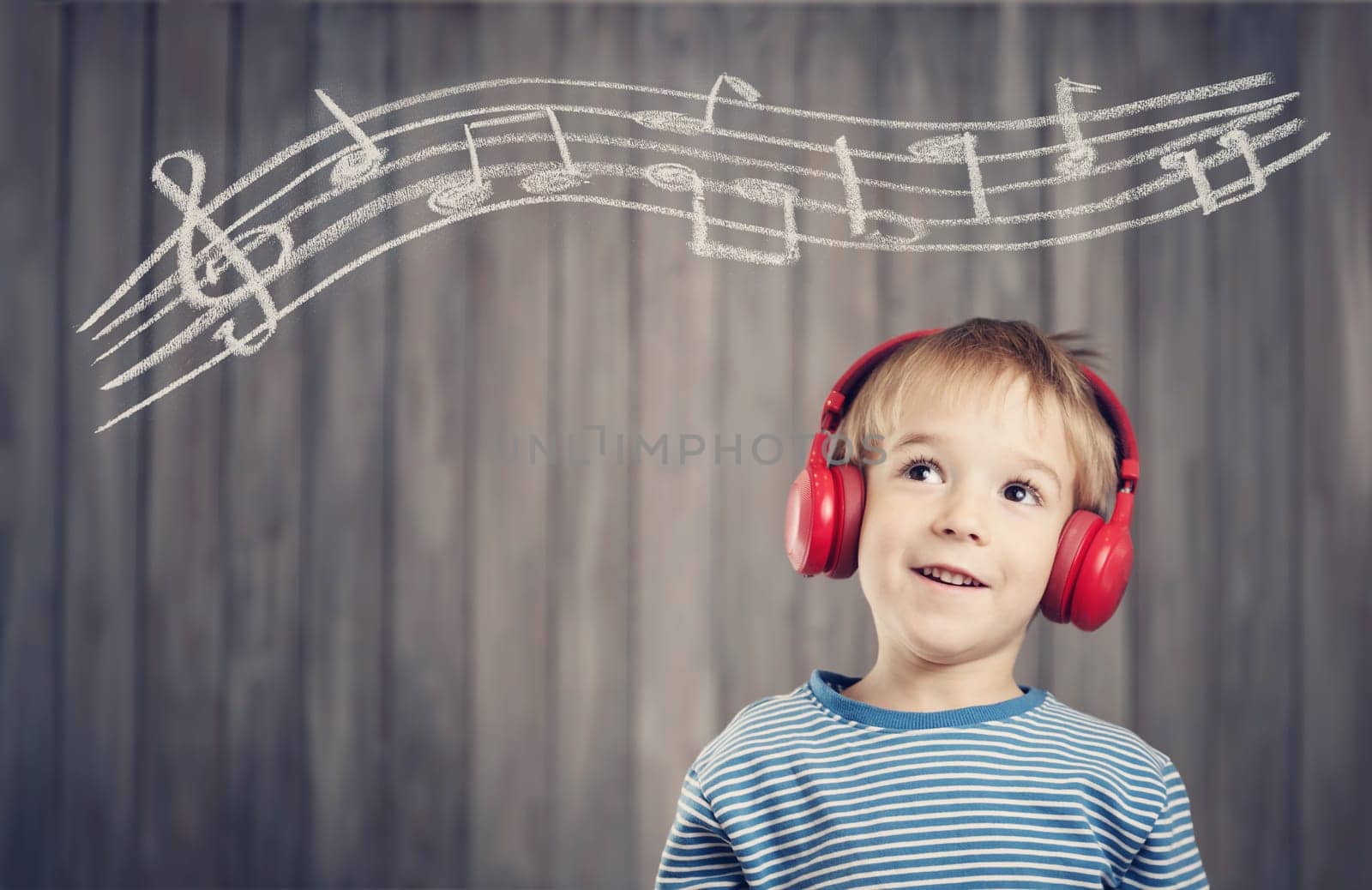 happy little boy on wooden background with red headphones. Child listening music with wireless headset. Musical concept with people