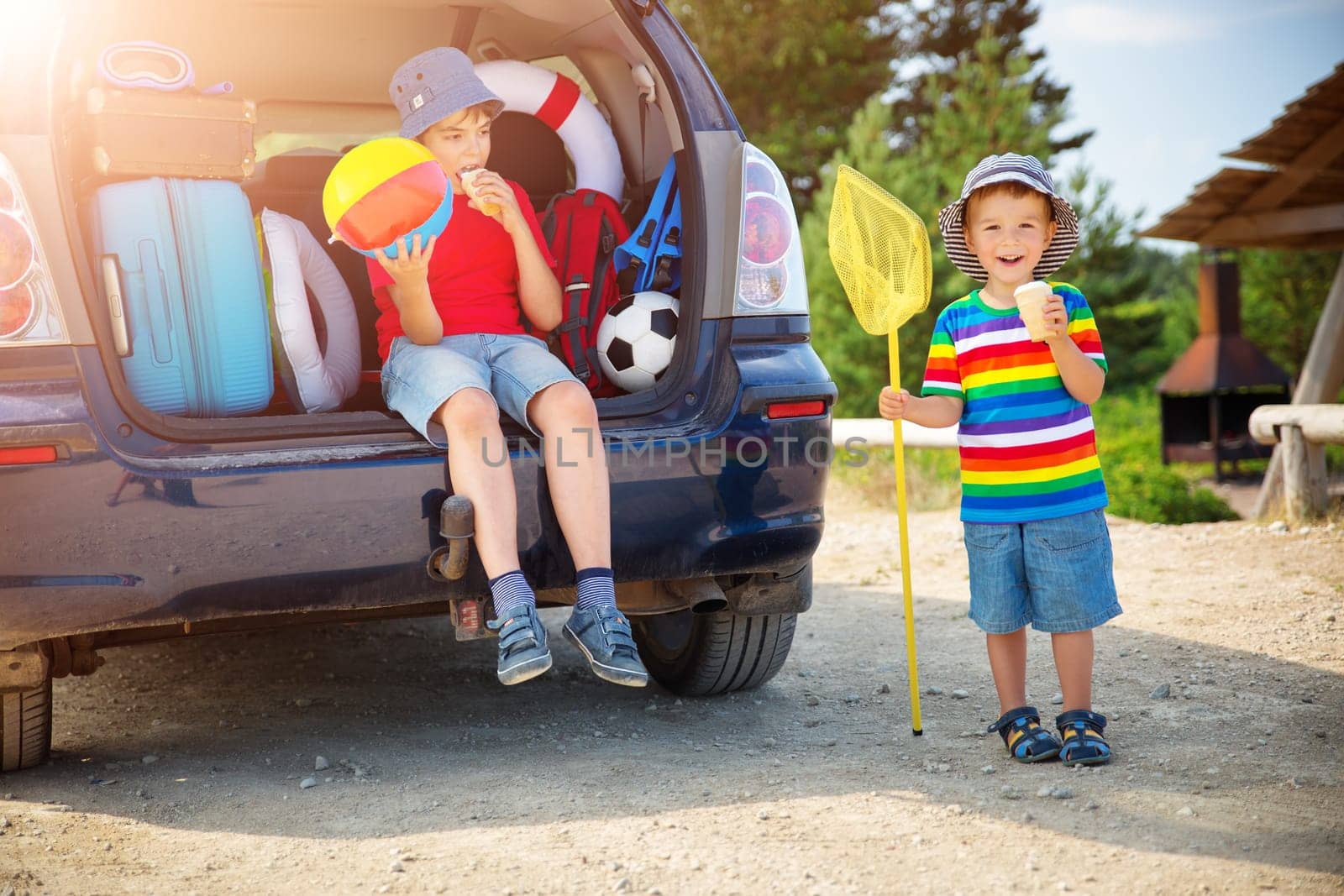Boy resting in nature in beautiful summer day. child sitting in car filled with traveling accessories and luggage. Travel and vacations concept