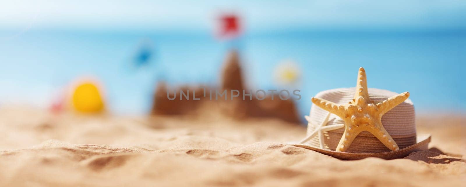 Sandcastle on the beach at sea in summertime. Seashore on beautiful day with clean sand, straw hat and starfish. Travel and vacations concept