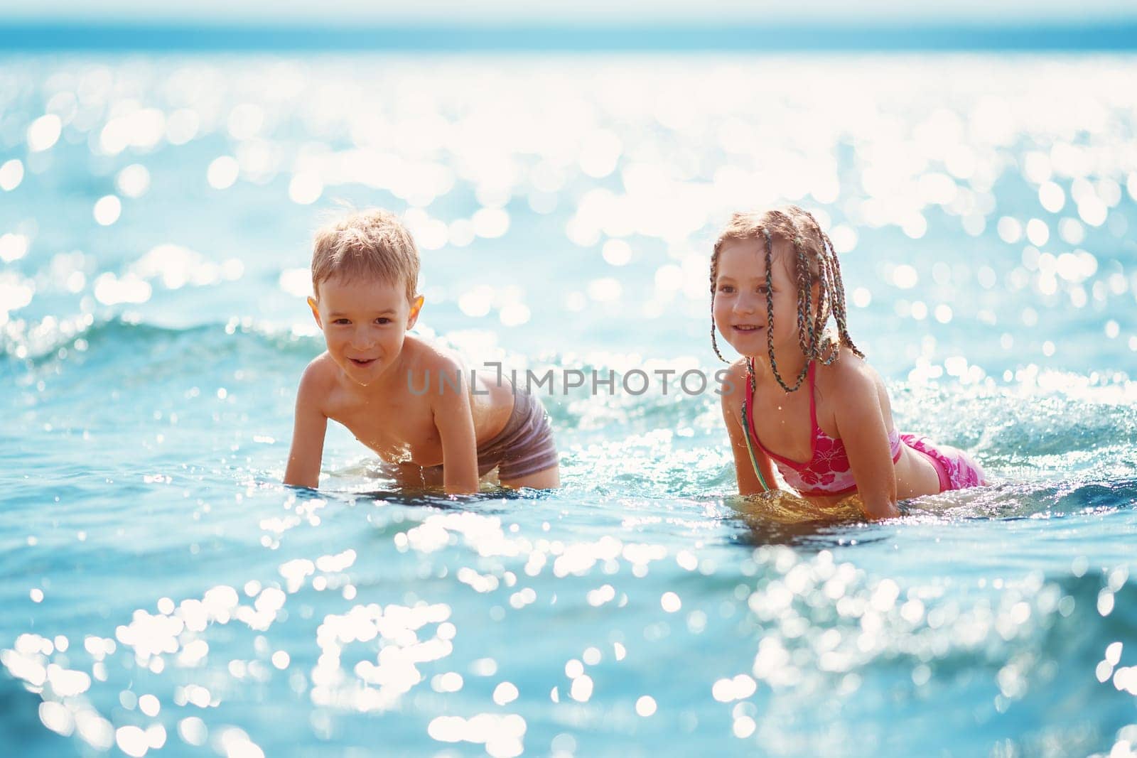 Boy and girl playing on the beach on summer holidays. Children in nature with beautiful sea, and blue sky. Happy kids on vacations at seaside splashing in the water