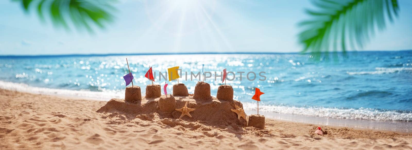 Sandcastle on the blue sea in summertime. Seashore with clean sand on beautiful day in summer. Tropical landscape with palm leaves. Vacations and travel concept