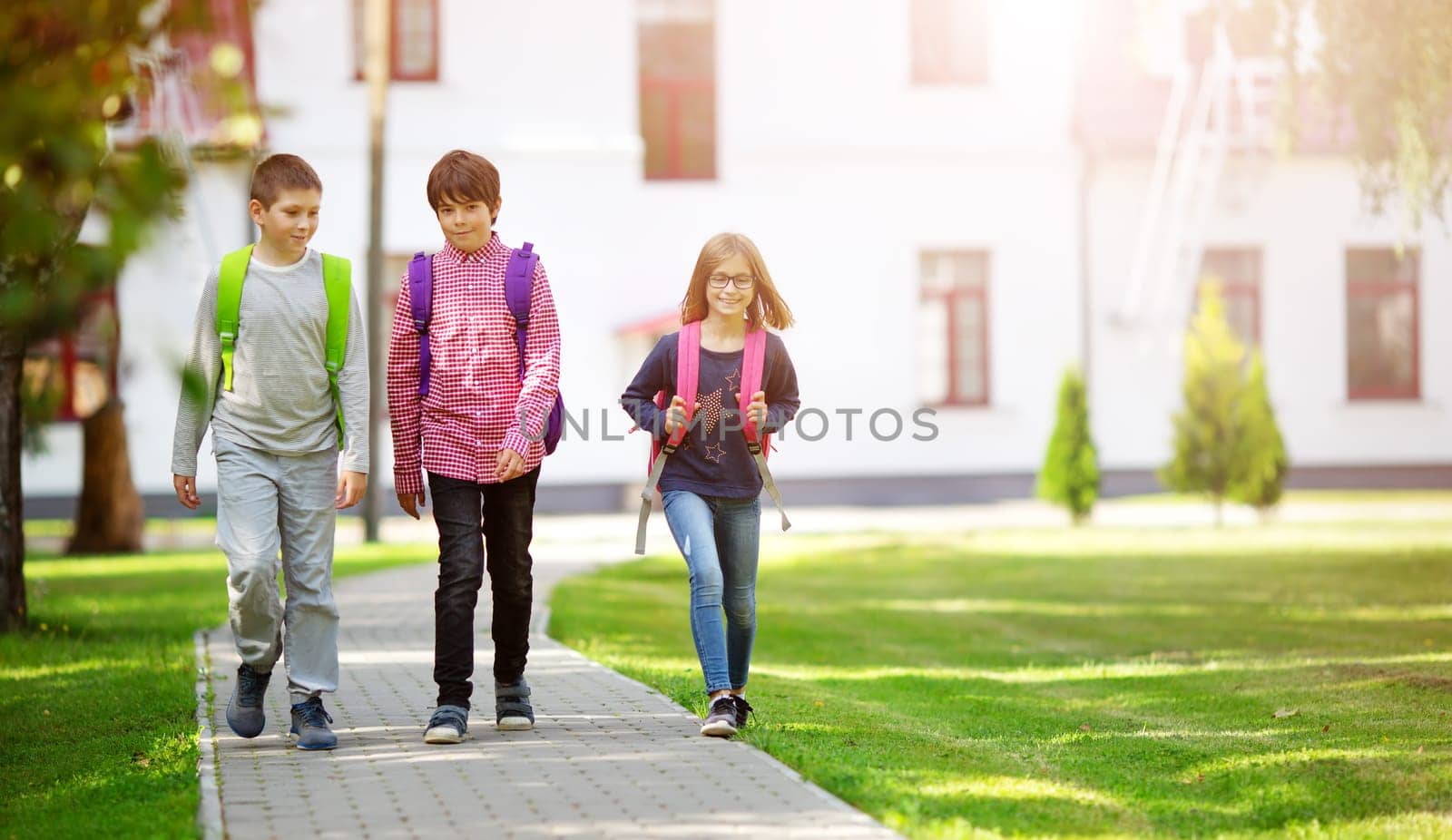 Children with rucksacks standing in the park near school. Pupils with books and backpacks outdoors