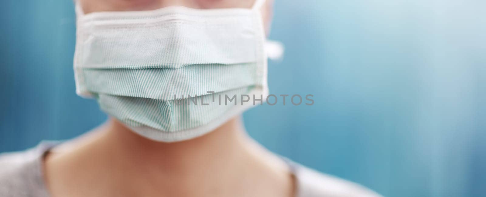 young woman in medical face protection mask indoors on blue background. Sick person