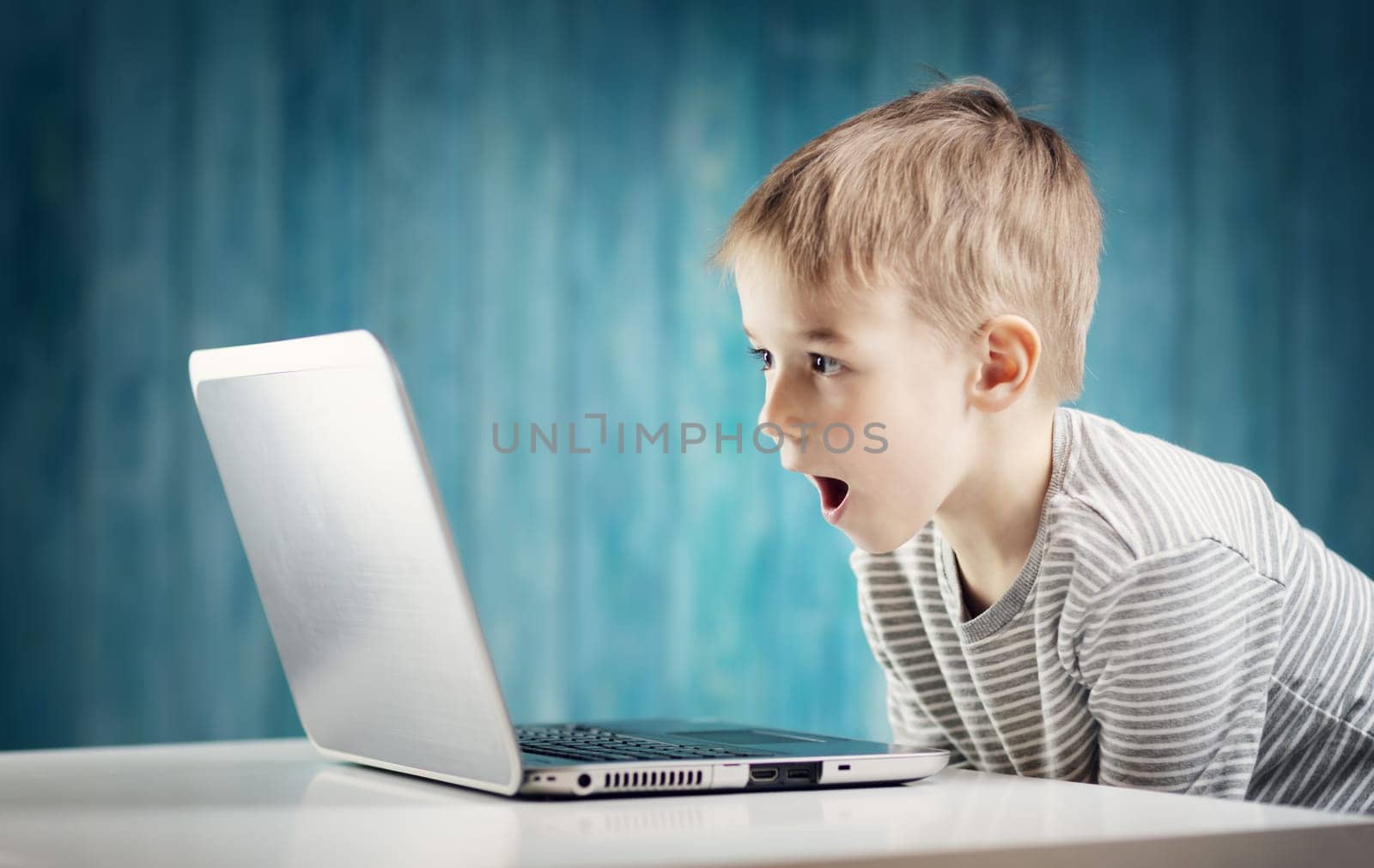 happy five years old child sitting with a laptop at table. Smiling boy working at personal computer