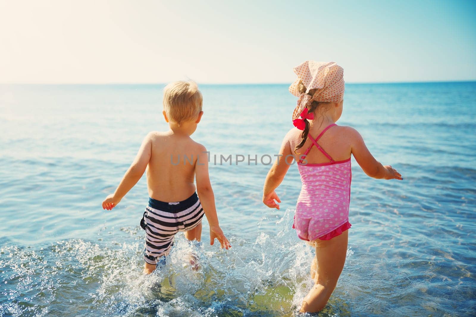 Boy and girl playing on the beach on summer holidays. Children in nature with beautiful sea, sand and blue sky. Happy kids on vacations at seaside running in the water