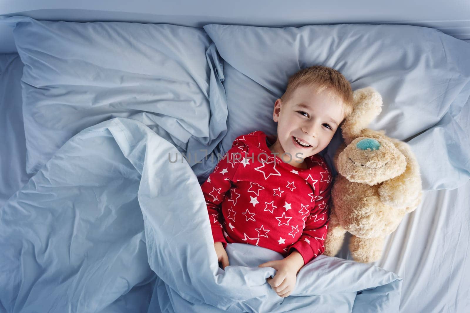 Sleepy boy lying in bed with white beddings. Tired child in bedroom sleeping. Little kid lying asleep with toy