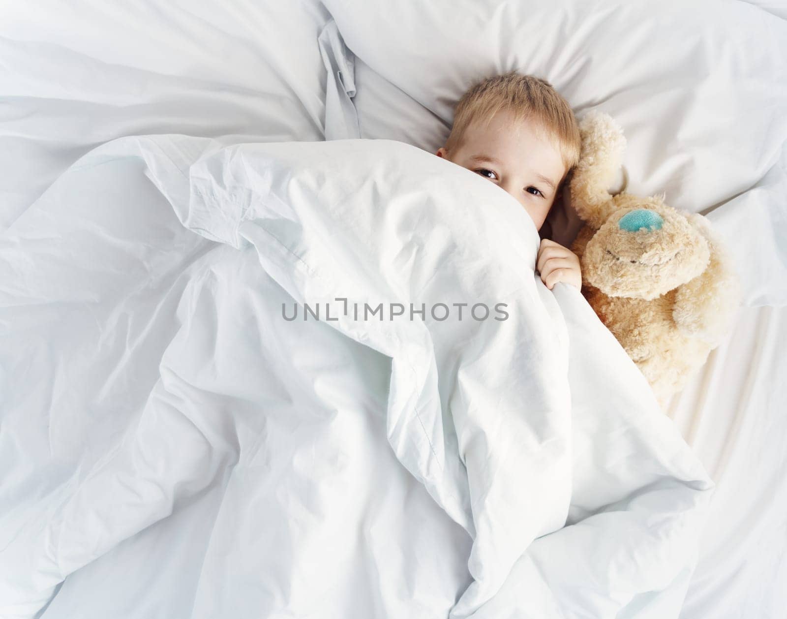 Sleepy boy lying in bed with white beddings. Tired child in bedroom sleeping. Little kid lying asleep with toy