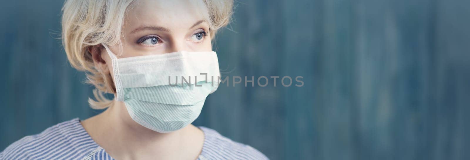 young woman in medical face protection mask indoors on blue background. Sick person