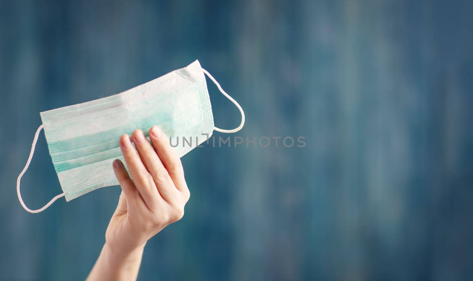 young woman holding face protection mask indoors on blue background. Sick person