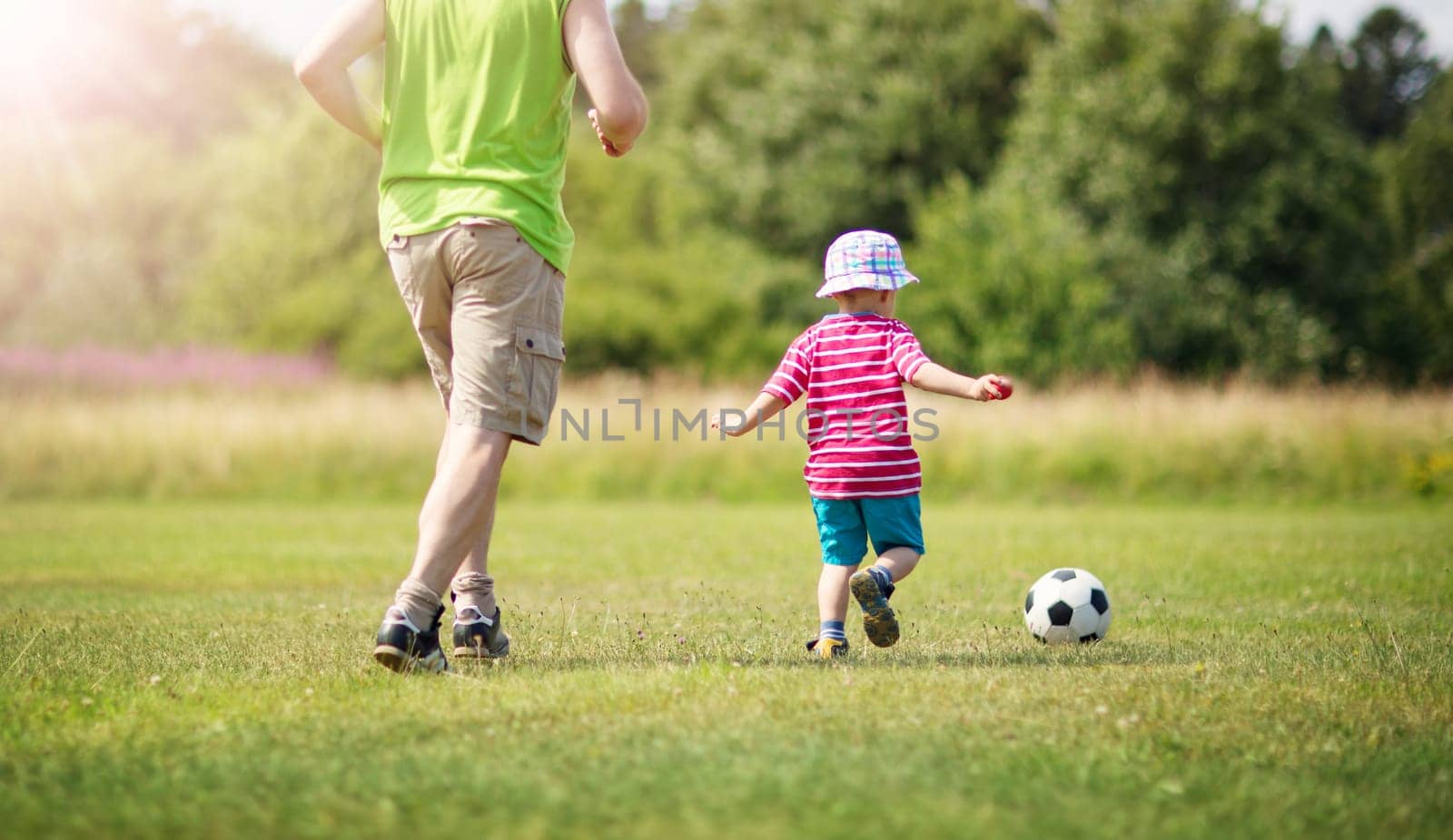 Little boy playting football on the field with gates. Active child in summer with ball