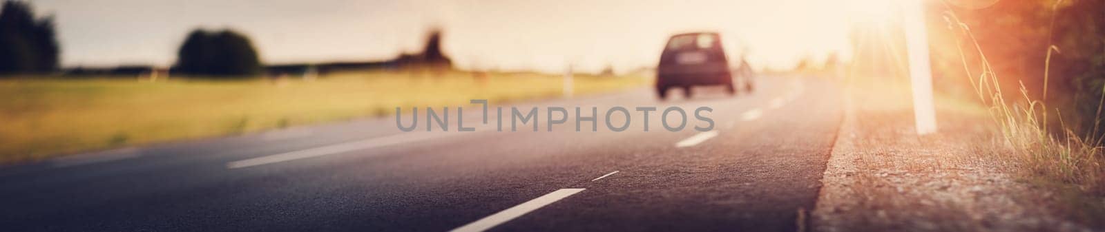 asphalt road view with a blurred car in countryside at beautiful sunset
