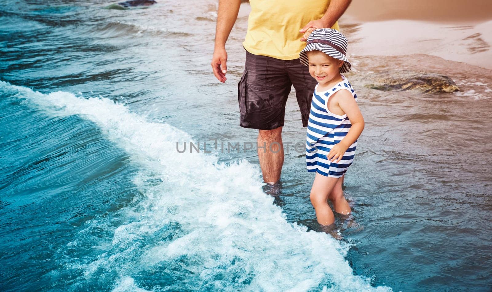 three years old boy with father playing at the beach in the water. Happy child and man on family vacations at sea in summer. Summertime tourism and travel concept