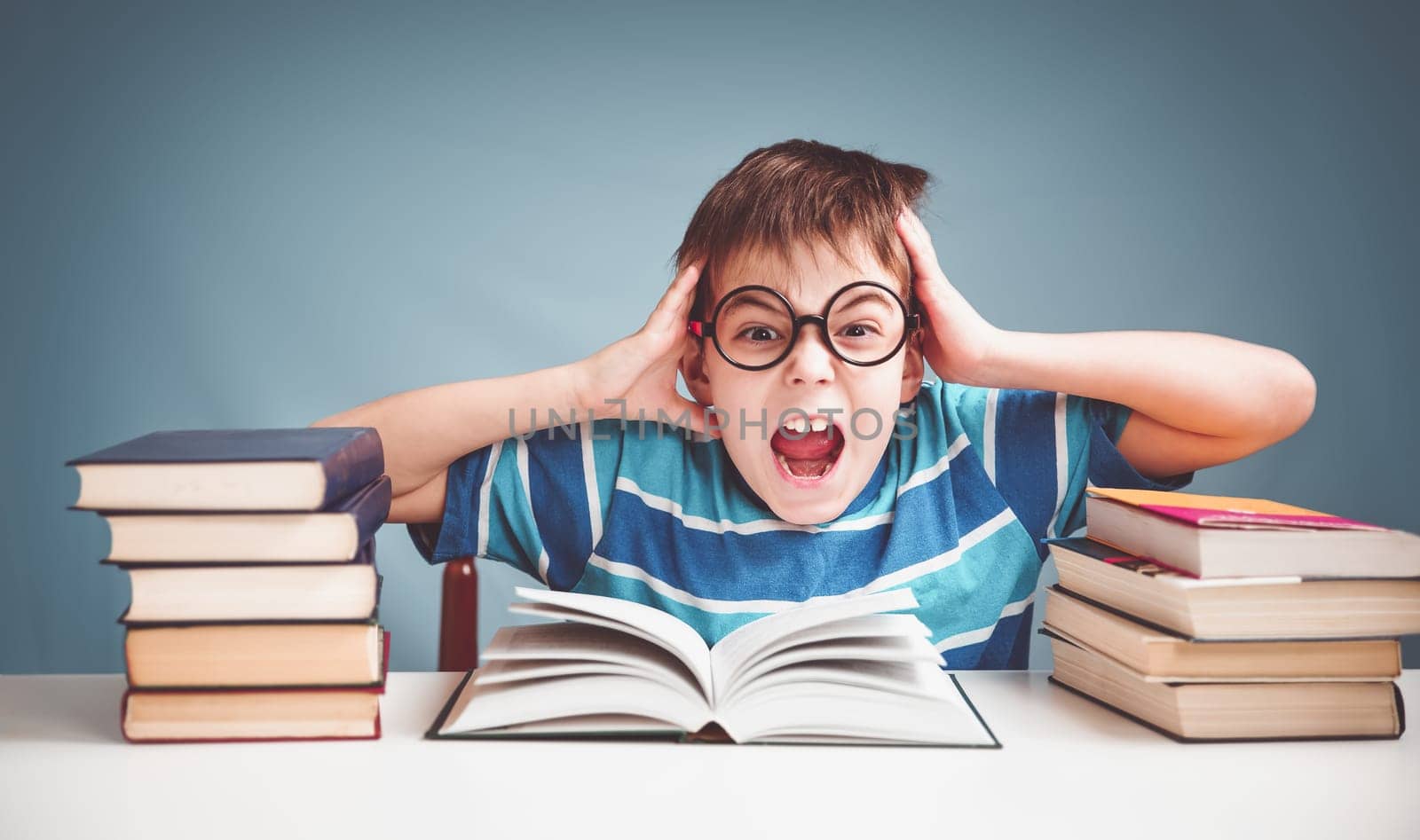 seven years old child reading a book at home. Boy studing at table on blue background