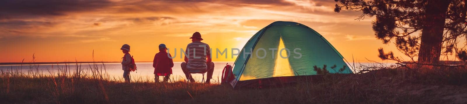 Family resting with tent in nature at sunset. Man and children near seaside