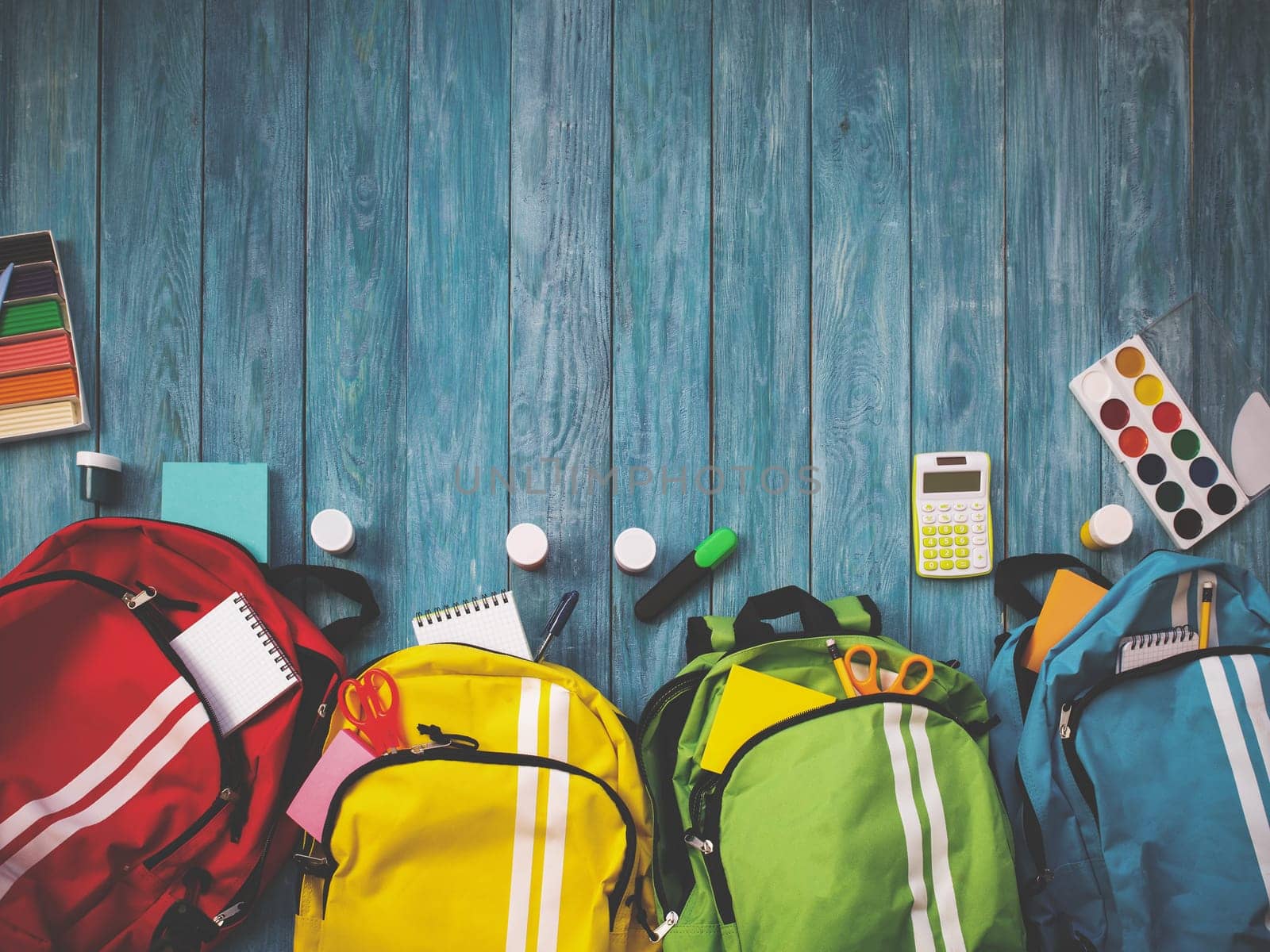 Colourful children schoolbags on wooden floor. Backpacks with school accessories