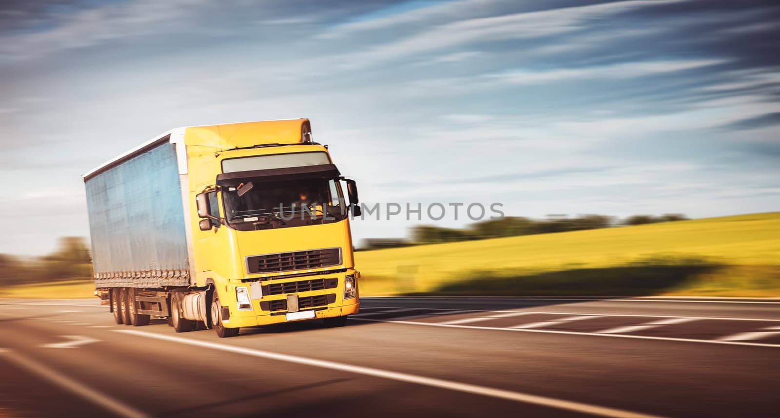 asphalt road on dandelion field with a small truck. lorry moving on sunny evening