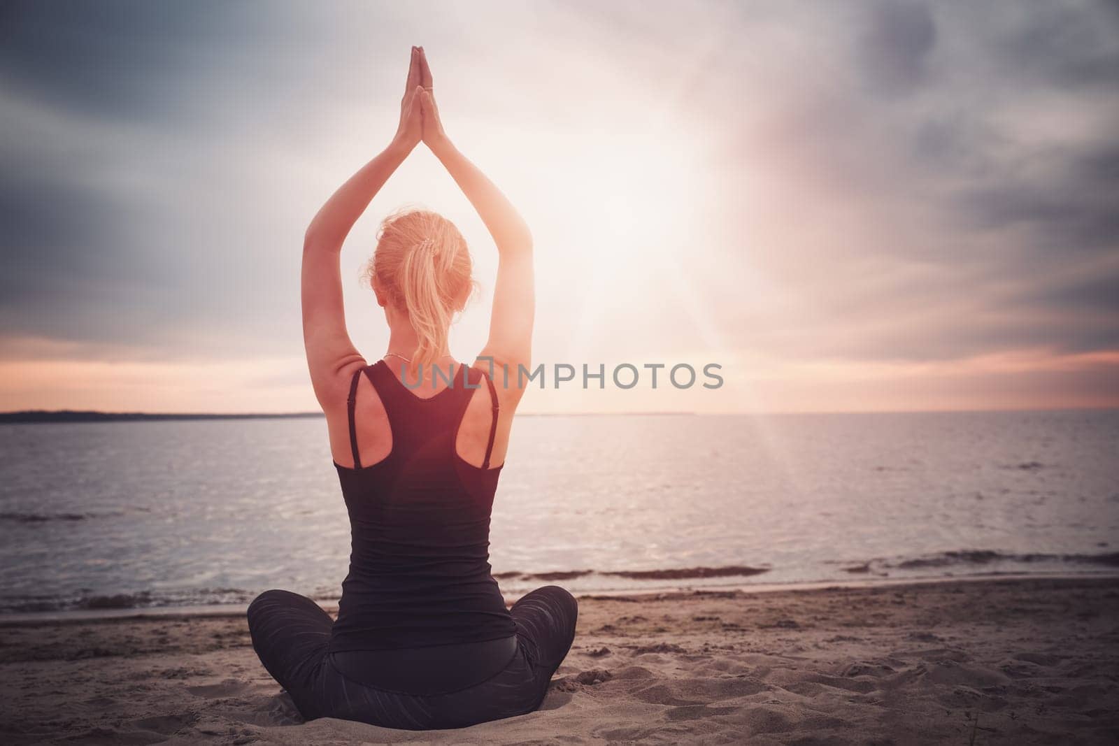 young woman sitting on the beach and practicing yoga