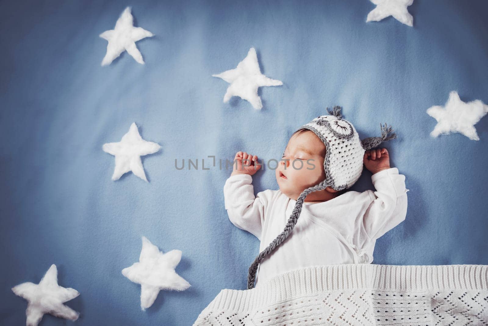 Cute newborn baby girl lying in the bed. 2 month old child in owl hat sleeping on blue blanket with stars