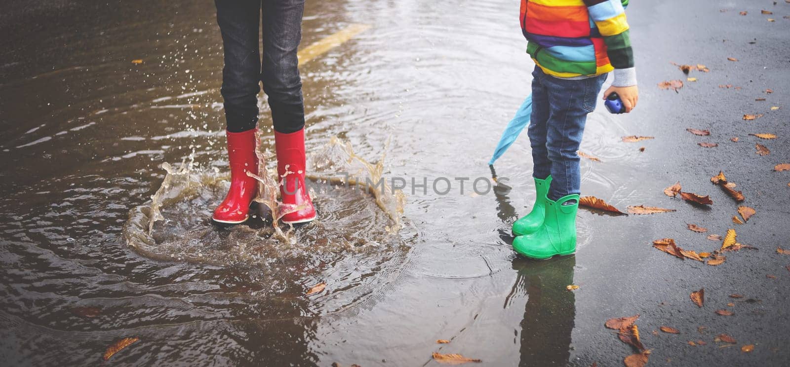 Child walking in wellies and jumping in puddle on rainy weather. Boy under rain in autumn outdoors