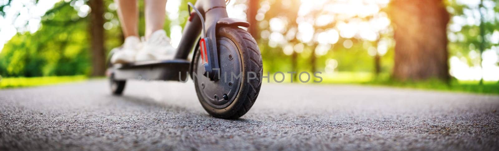 Woman riding on scooter in park in summer. Urban eco transportation