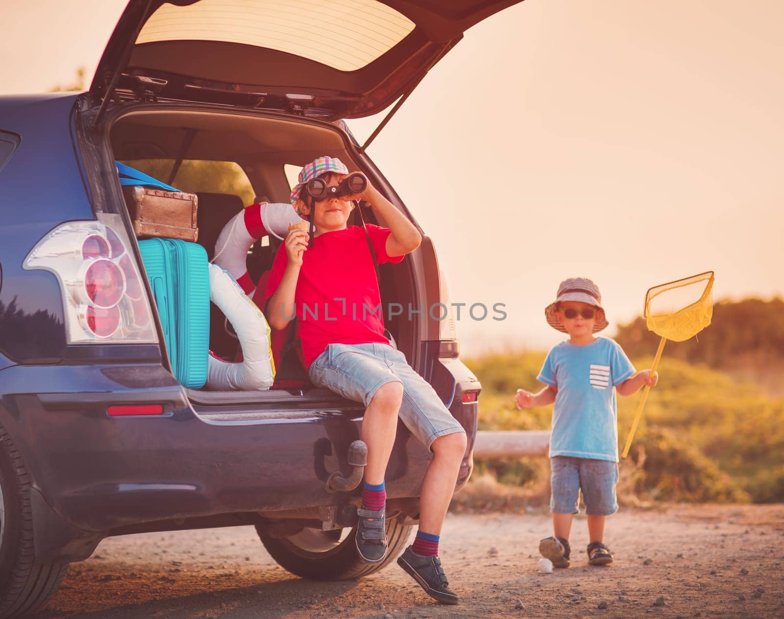 Boy resting in nature at sunset. child sitting in car filled with traveling accessories