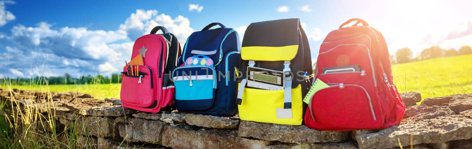 Colourful children schoolbags outdoors on the field. Backpacks with school accessories