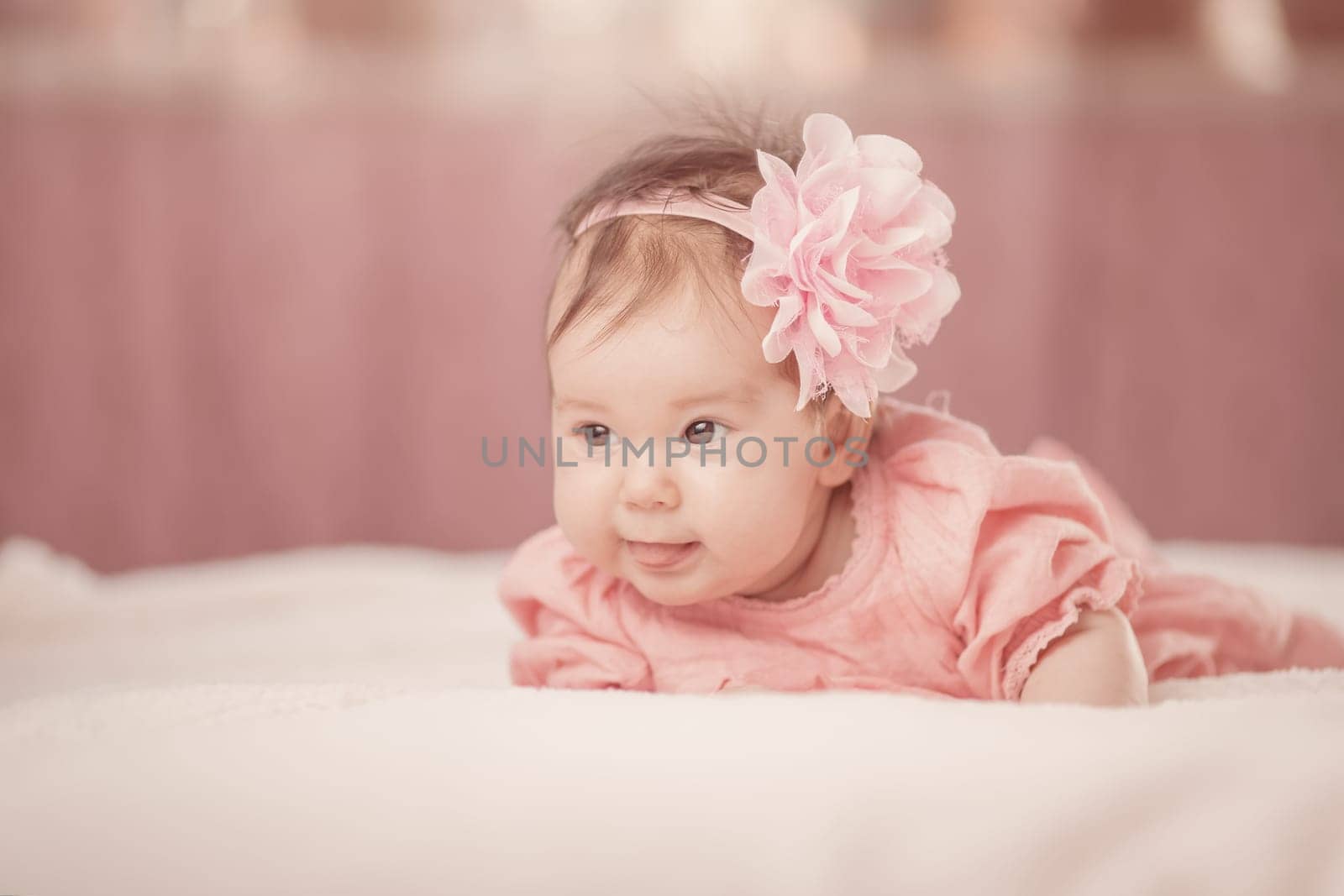 Cute little baby girl lying in the bed in pink dress. Three month old infant child on white soft blanket