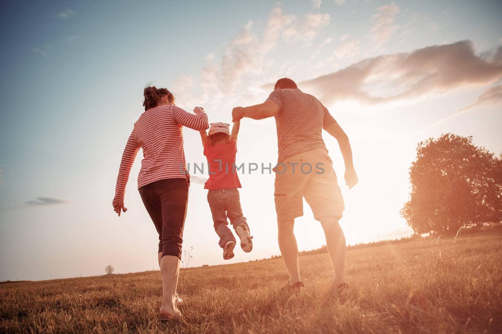 girl with mother and father holding hands on the nature. Child with parents outdoors