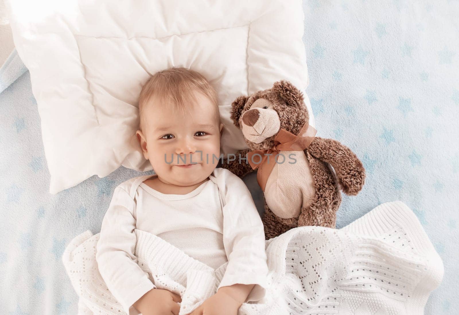 One year old baby lying in bed with a plush teddy bear