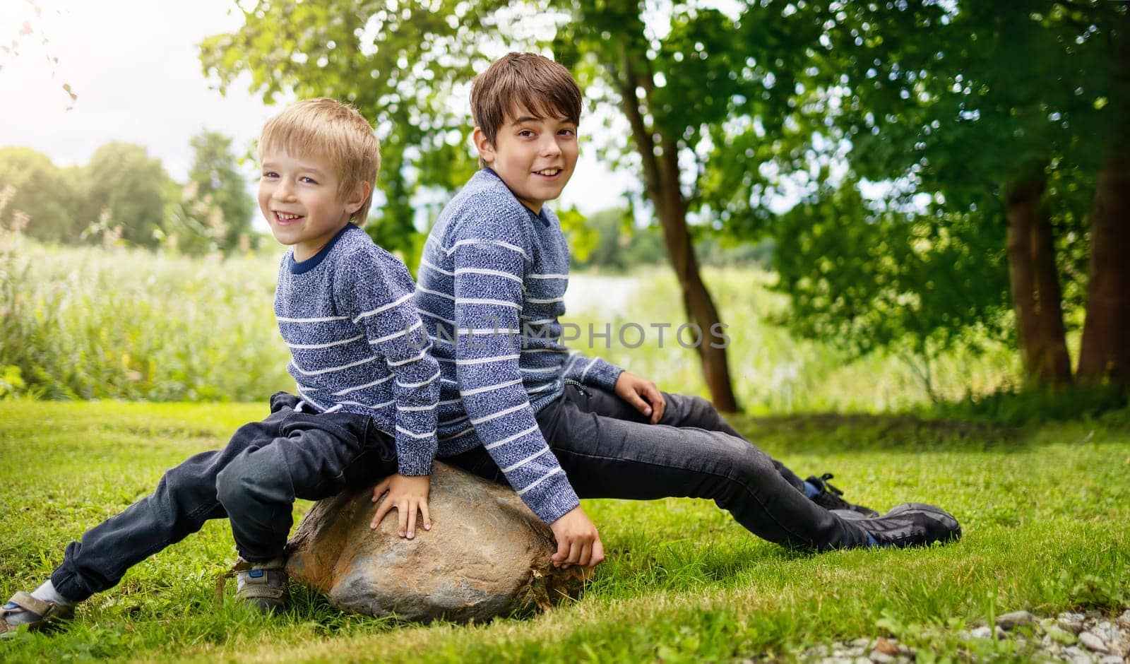 Two lovely happy brothers sitting in park. Boys outdoors in nature