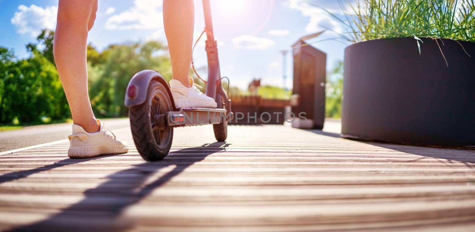 Woman riding on scooter in park in summer. Urban eco transportation