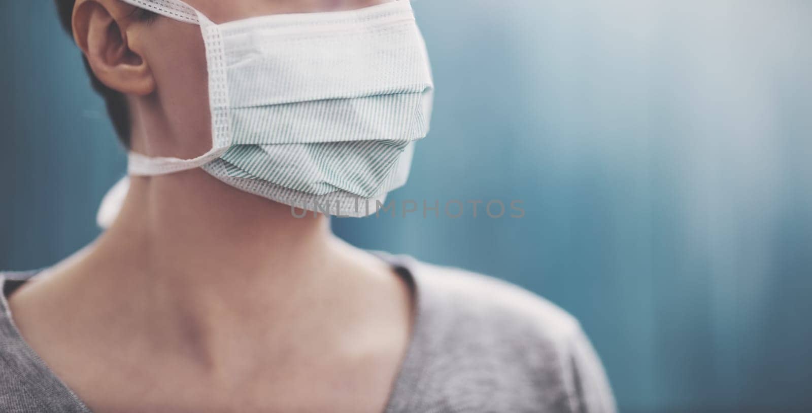 young woman in medical face protection mask indoors on blue background. Sick person