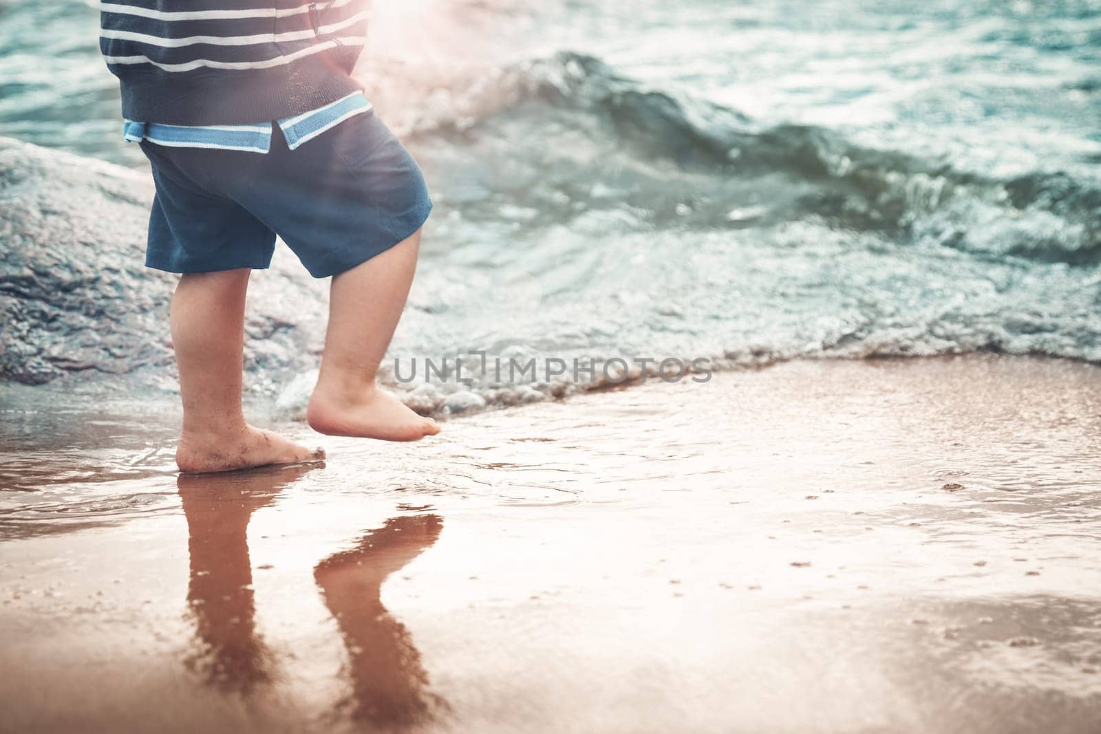 Baby boy barefoot are walking on the beach in water. Child on vacation in summer at the sea on bad weather