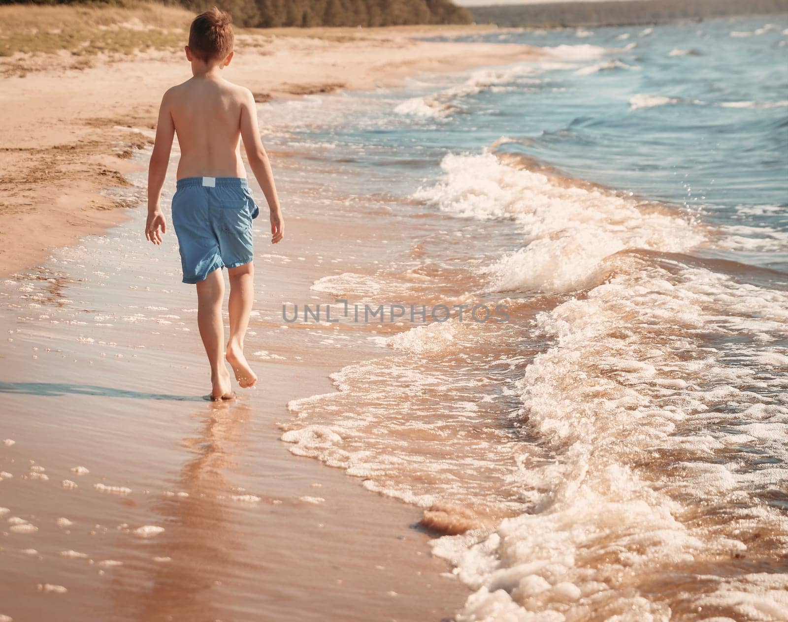 boy barefoot is jumping on the beach in water. Child is on vacation in summer at the sea