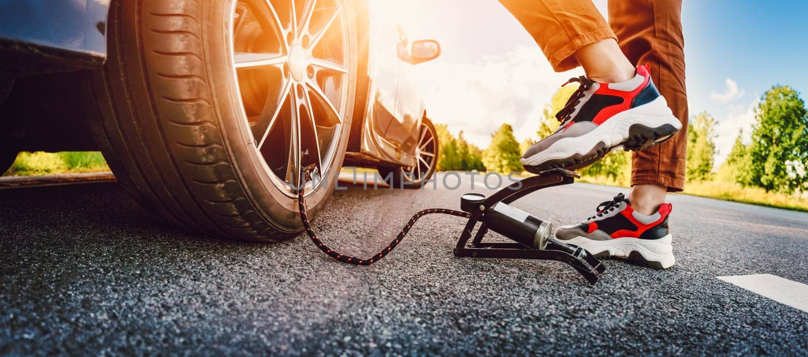 Driver using a foot pump to inflate a tire. Woman near car wheel outdoors