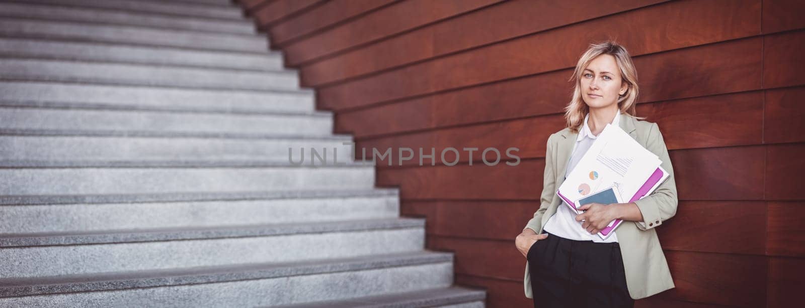 young woman with laptop standing on the stairs. Person with personal computer and documents outdoors