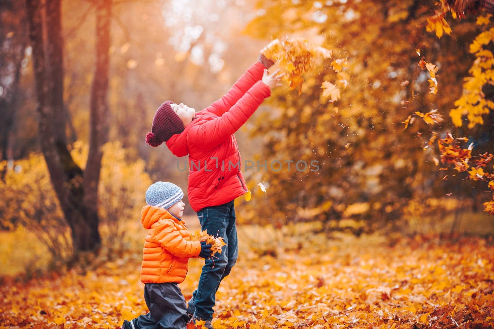 children throwing leaves in beautiful autumnal day. Boys playing outdoors in the park