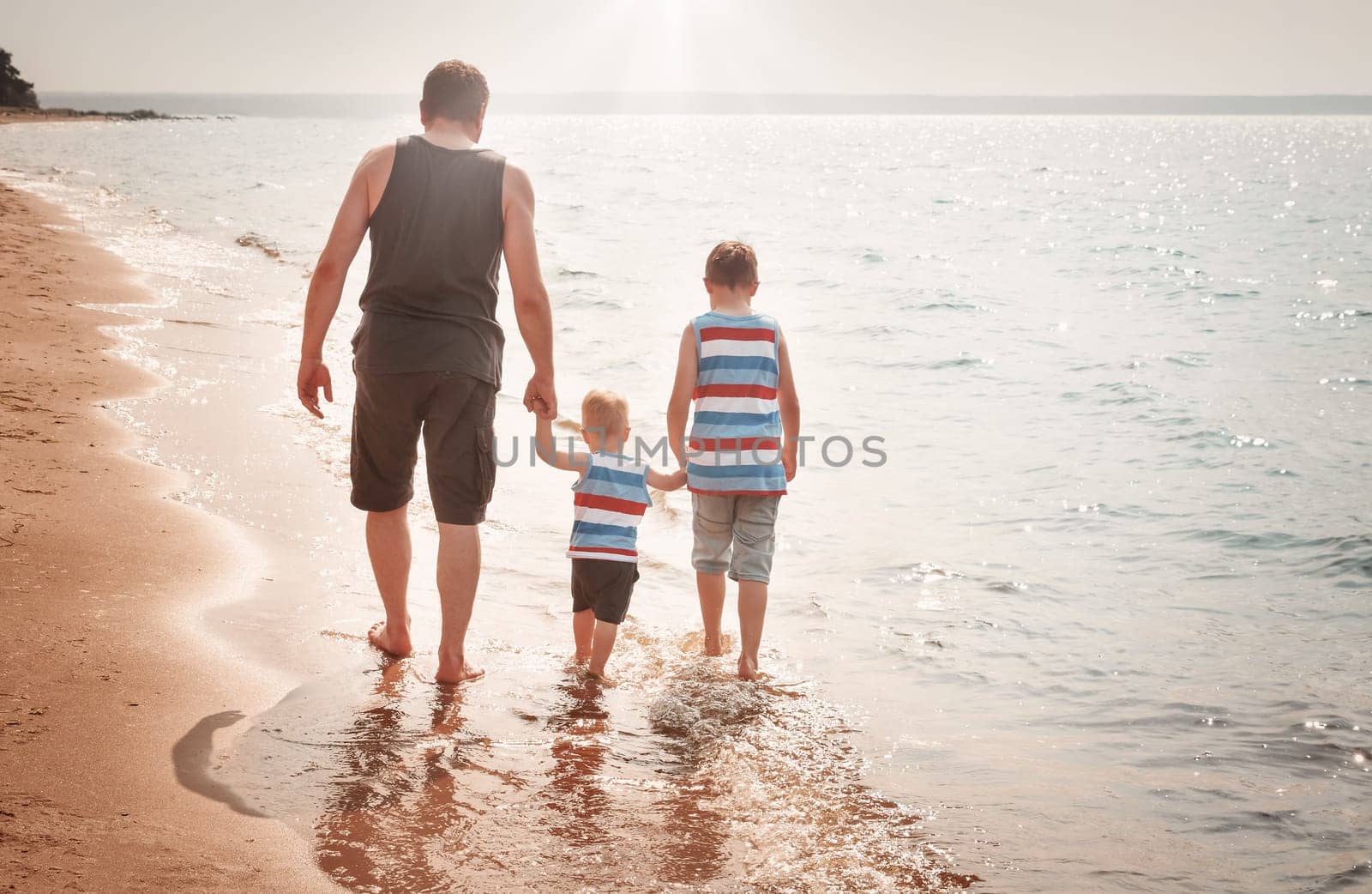 Father and sons walking at the beach at sea. A man with children resting at seaside in summer on sunny day